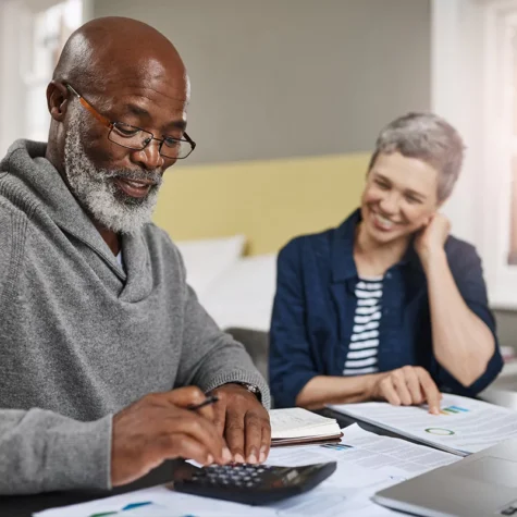 Two individuals at a table with documents and a calculator, possibly managing finances.